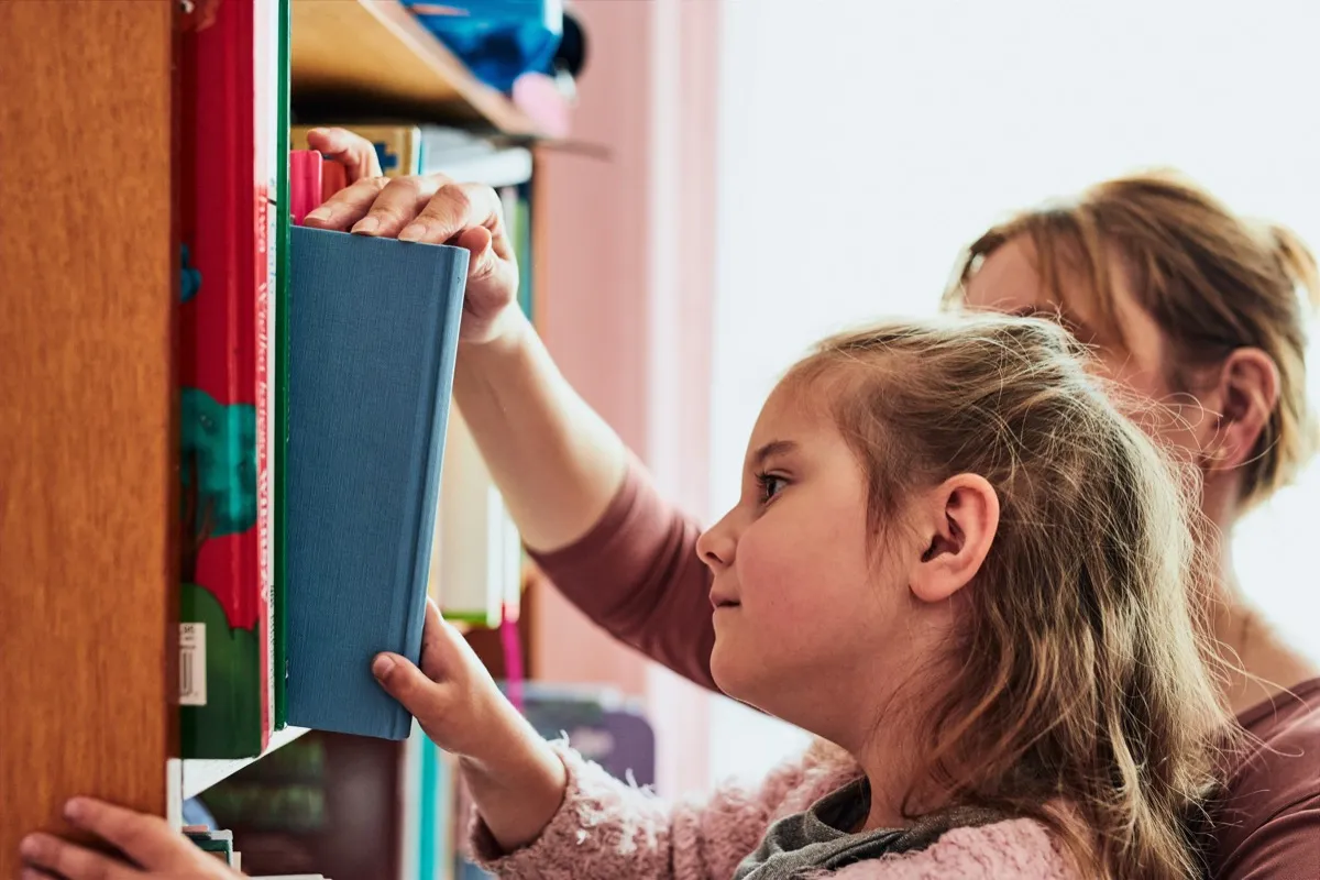 A young student picking a book from a library shelf