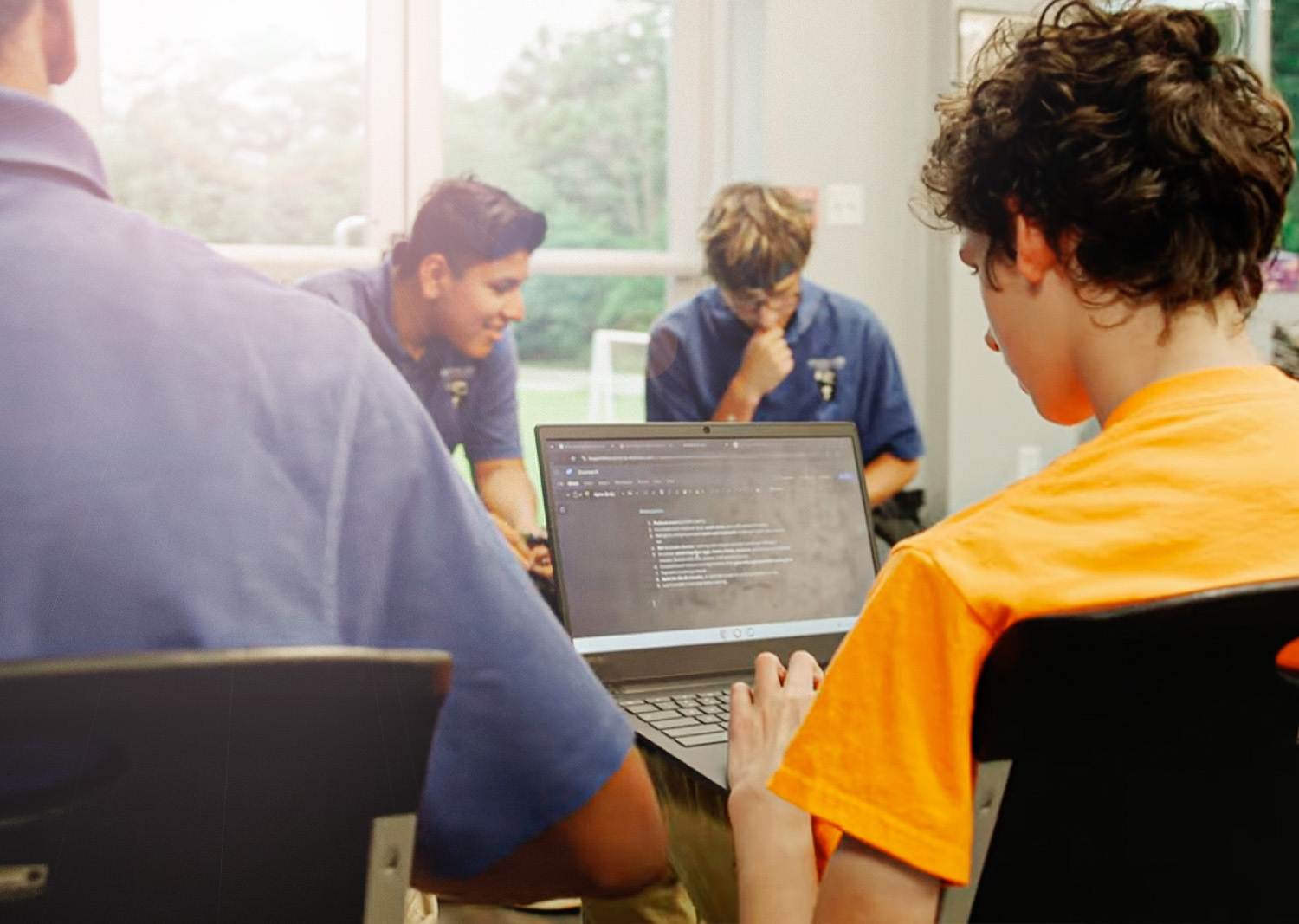 Students seated around a table working together on laptops in a Kingdom Life Academy classroom setting.