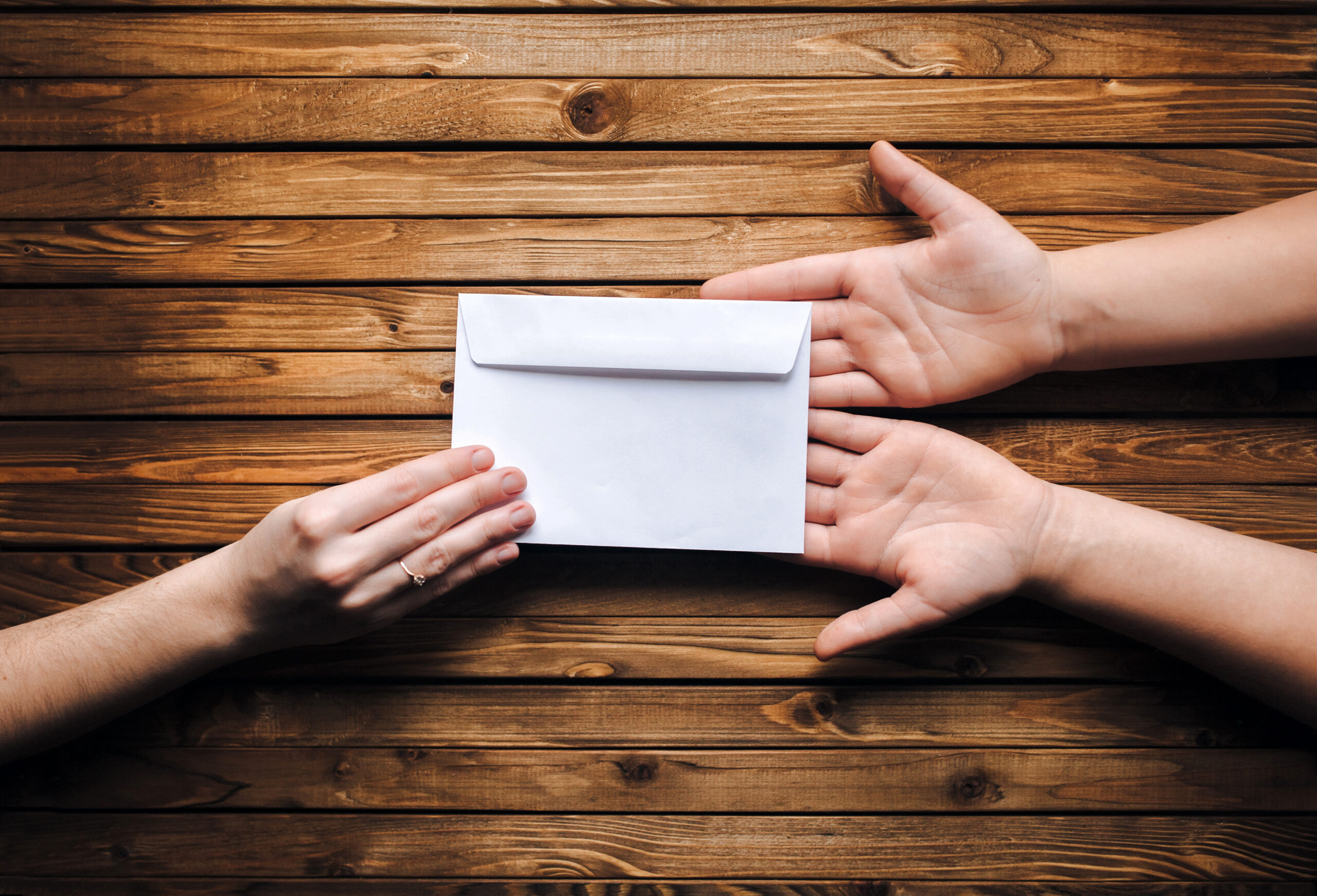 Hands exchanging an envelope over a wooden table